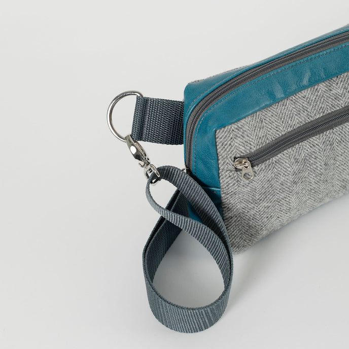 A gray strap with silver tone hardware on a wool errand with teal accents