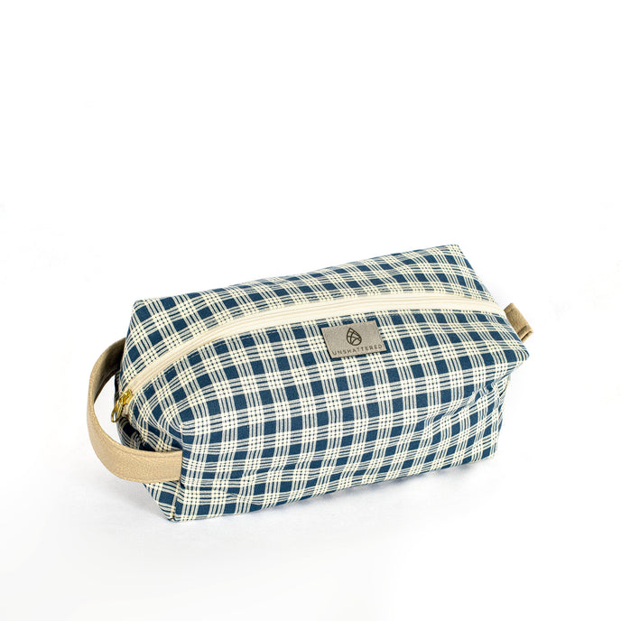 A blue and white plaid toiletry kit with a tan zipper and hardware, displayed against a white background.