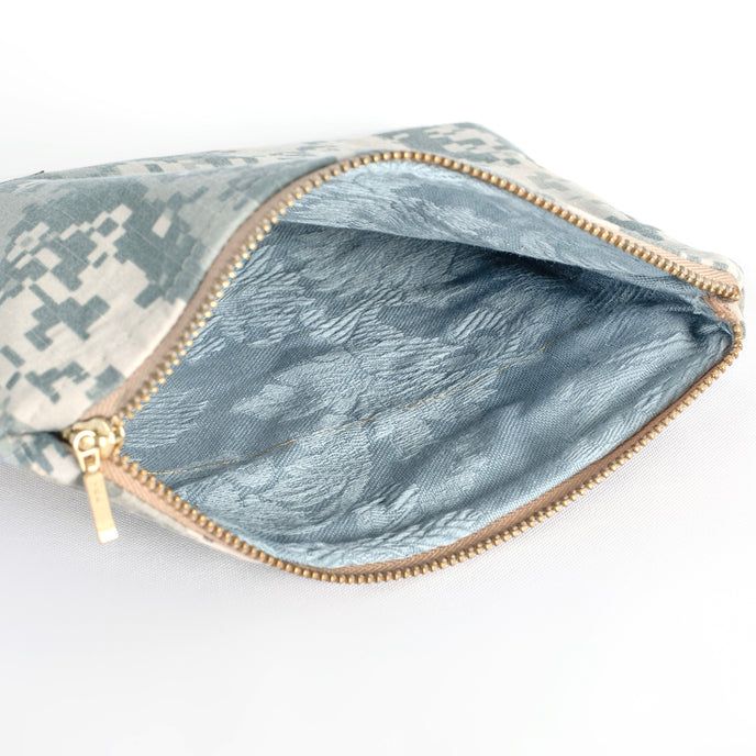 A blue floral fabric interior with a gold seam on a zip pouch handcrafted from an upcycled US Army military uniform with a gold tone zipper 