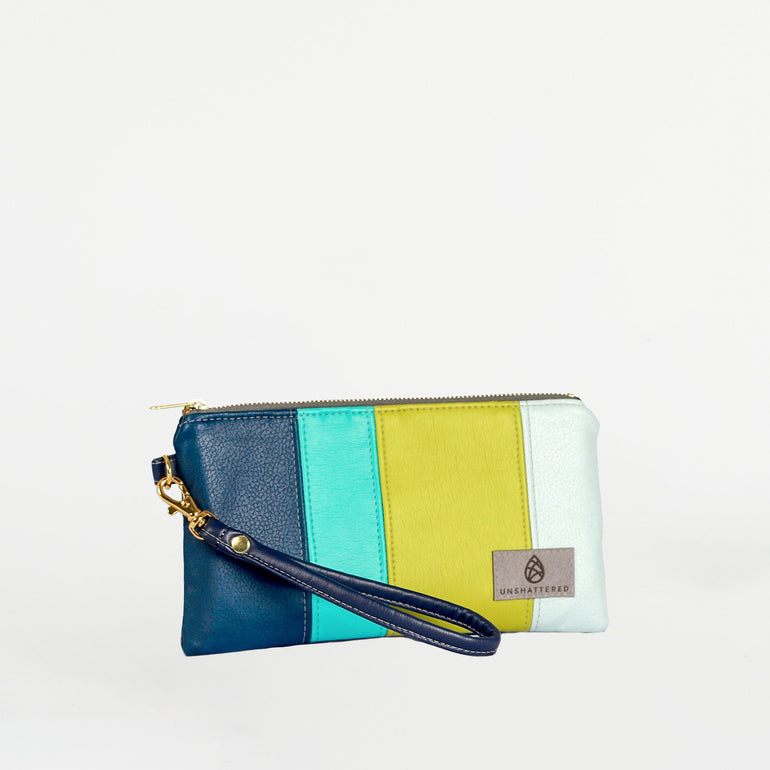 A multicolored wristlet with a detachable strap, featuring a navy blue, green, and yellow color scheme with a brand logo on the bottom right.