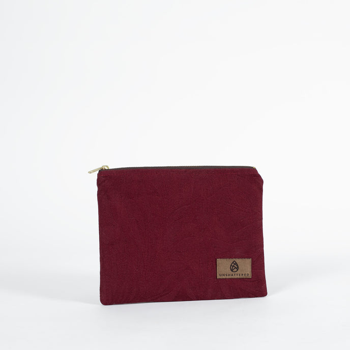 A burgundy floral demask zip pouch with a brown label on a white background