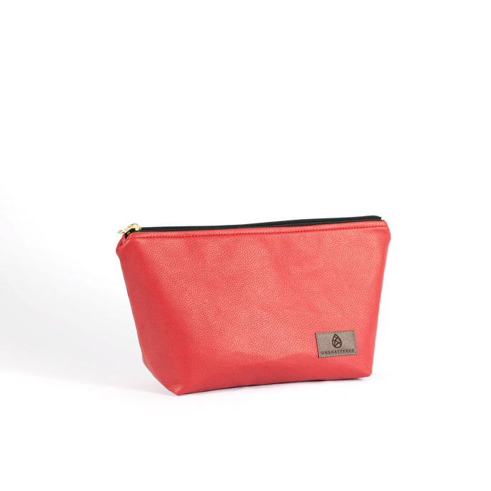 A bright red makeup bag handcrafted from upcycled materials with a black zipper and gold hardware on a white background