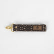 This brown fabric wristlet key clip features a playful dotted pattern and sleek gold-tone hardware.