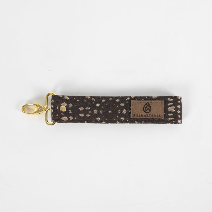 This brown fabric wristlet key clip features a playful dotted pattern and sleek gold-tone hardware.