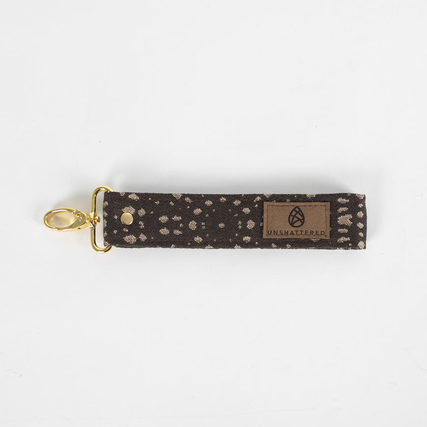 This brown fabric wristlet key clip features a playful dotted pattern and sleek gold-tone hardware.