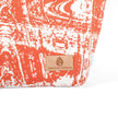 Tan suede Unshattered label on a orange and white makeup bag on a white background