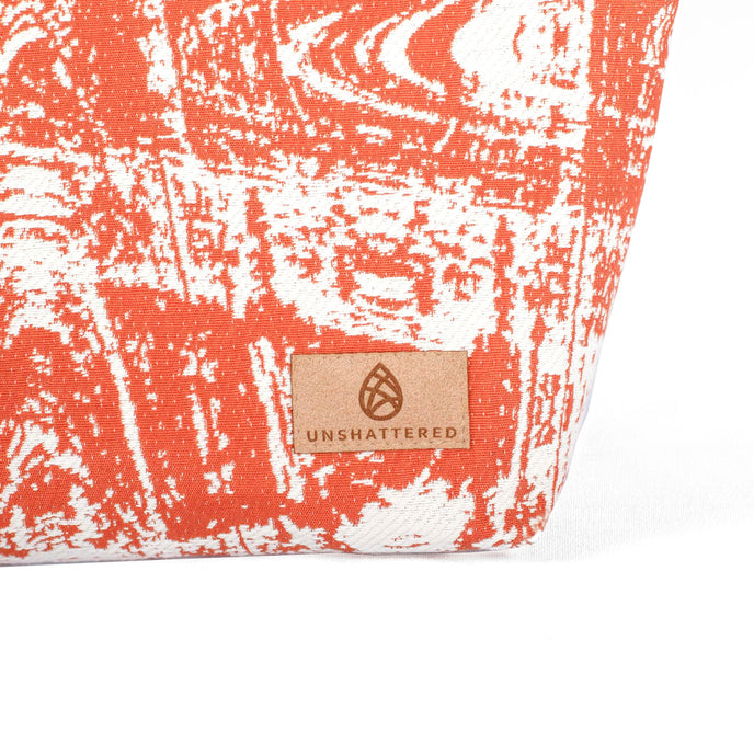 Tan suede Unshattered label on a orange and white makeup bag on a white background