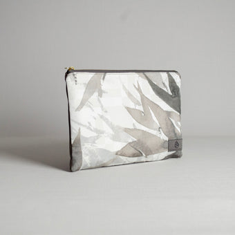 A large zip pouch with a geometric pattern in shades of gray, with gold-tone hardware and a fabric label showing the brand name.