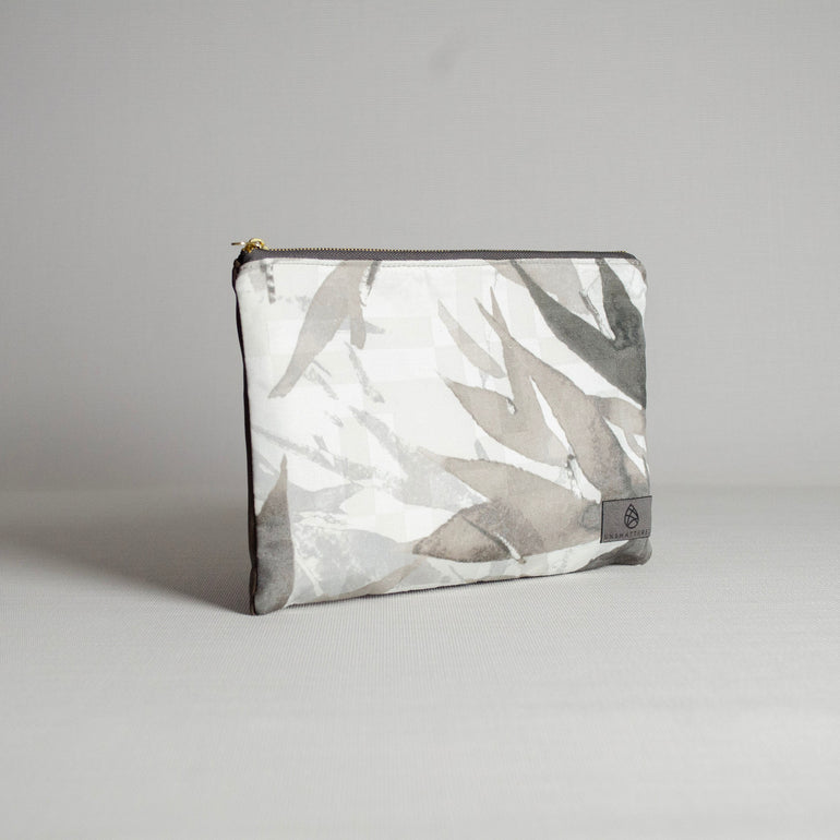 A large zip pouch with a geometric pattern in shades of gray, with gold-tone hardware and a fabric label showing the brand name.