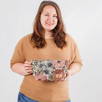 A woman holding a floral makeup kit with a tan Unshattered label 