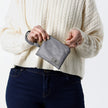 A woman opening a gray-blue clip pouch with a removable wristlet strap and gold-tone hardware, zippered closure, displayed against a white background named after Camille.