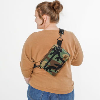 Person wearing a camouflage crossbody bag on a white background