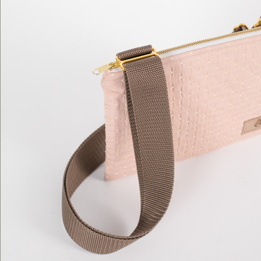 Detail shot of the gold hardware on a pink and yellow dotted crossbody pouch with a brown strap 