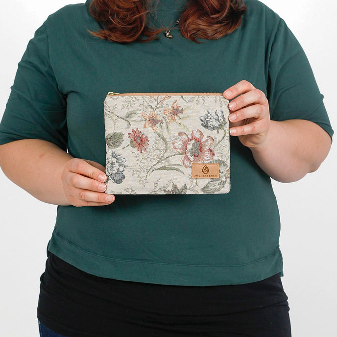 woman holding a floral zip pouch with a tan Unshattered label named after Cathy