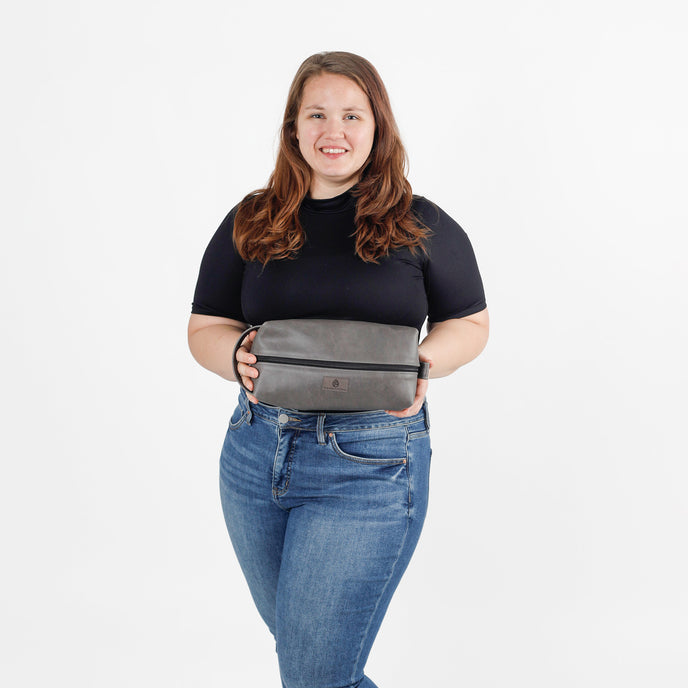 Woman holding a gray leather toiletry kit against a white background