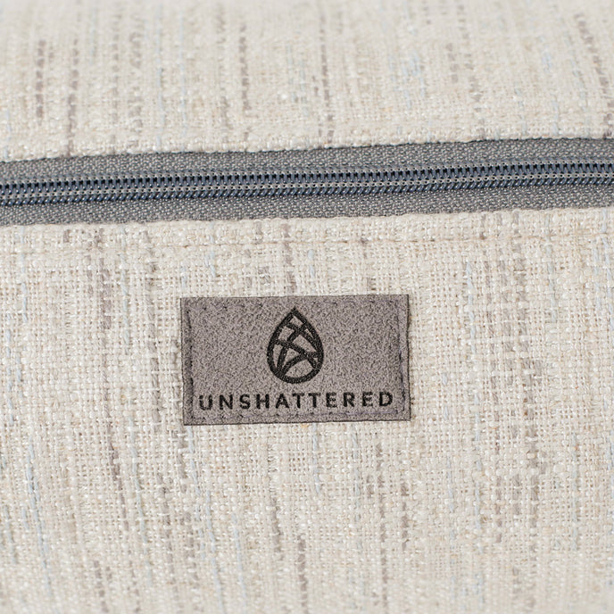 Close-up of a textured fabric toiletry bag with a zipper and 'Unshattered' suede label