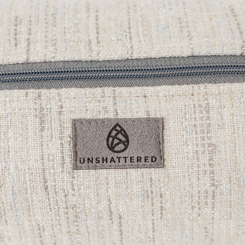 Close-up of a textured fabric toiletry bag with a zipper and 'Unshattered' suede label