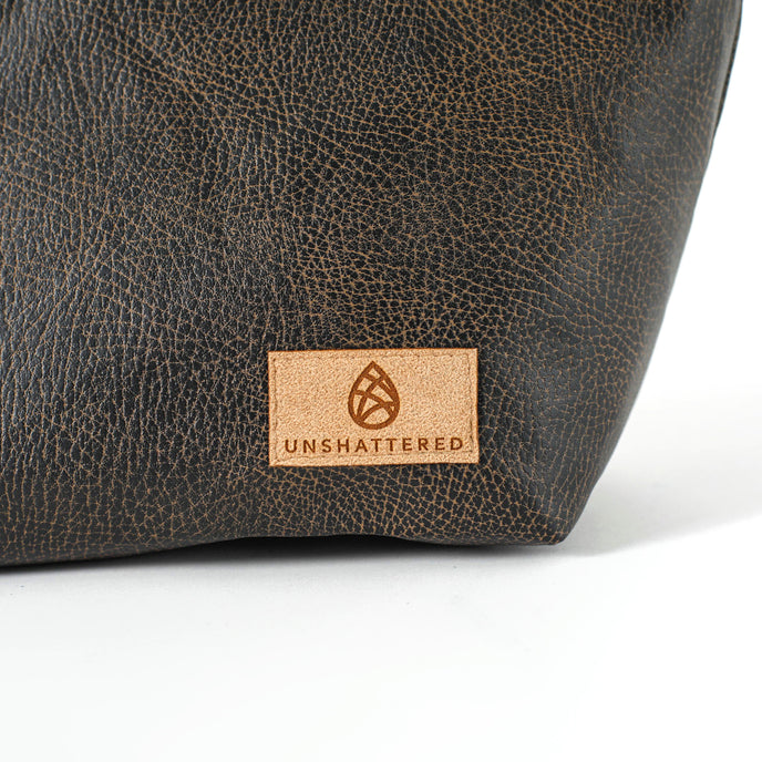 Close up of a tan suede Unshattered label on a brown luxury leather alternative makeup bag