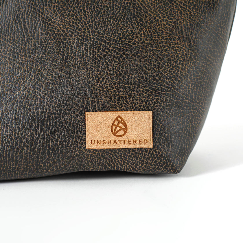 Close up of a tan suede Unshattered label on a brown luxury leather alternative makeup bag