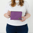 Person holding a purple pouch with a visible brand logo on a white background named after Connie 