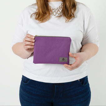 Person holding a purple pouch with a visible brand logo on a white background named after Connie 