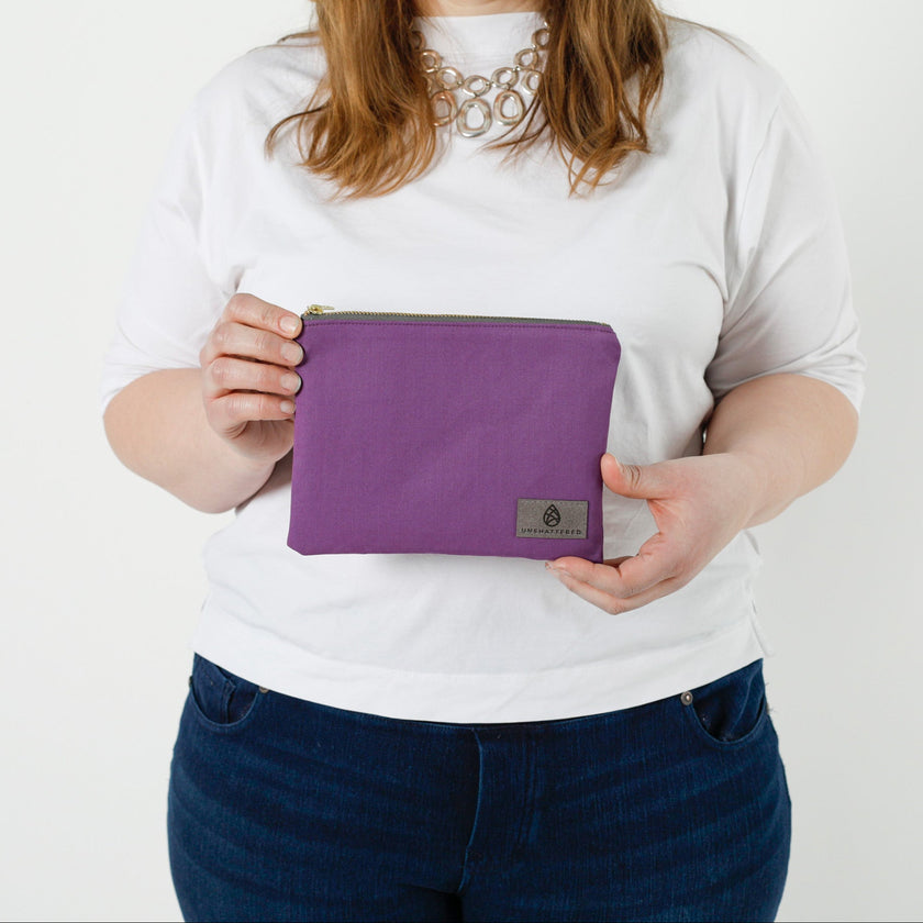 Person holding a purple pouch with a visible brand logo on a white background named after Connie 