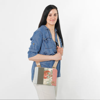A woman carrying a crossbody pouch with a floral design on the front, featuring a mix of upcycled materials in multicolor, with a beige adjustable strap and gold-tone hardware named after Julie 