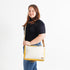 Woman holding a yellow and white convertible handbag on a white background