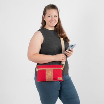 A woman smiling while wearing a versatile 3-in-1 crossbody bag featuring a vibrant red and sunflower floral pattern, holding a cell phone to demonstrate the hands-free convenience of the style.