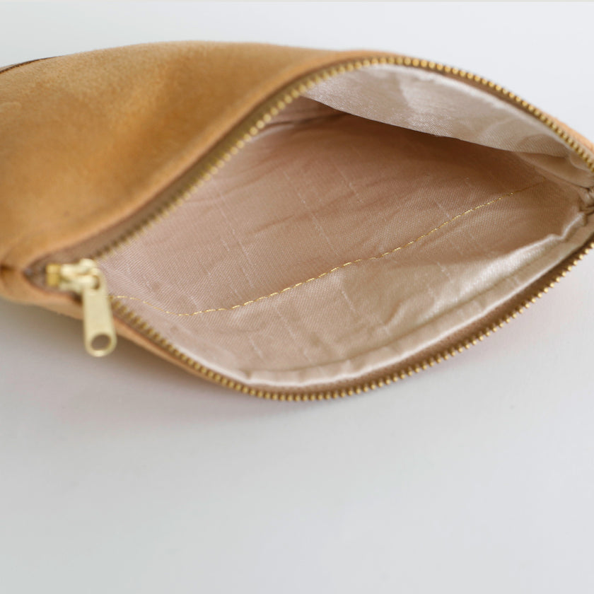 Interior of beige suede pouch with gold zipper on a light gray background