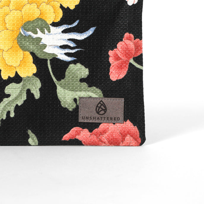 Gray suede Unshattered label on an upcycled floral-patterned fabric pouch named Felicia 