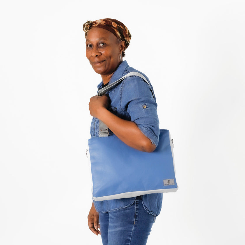 A woman wearing a blue luxury leather alternative handbag with gray straps and silver toned hardware named after Diamond 