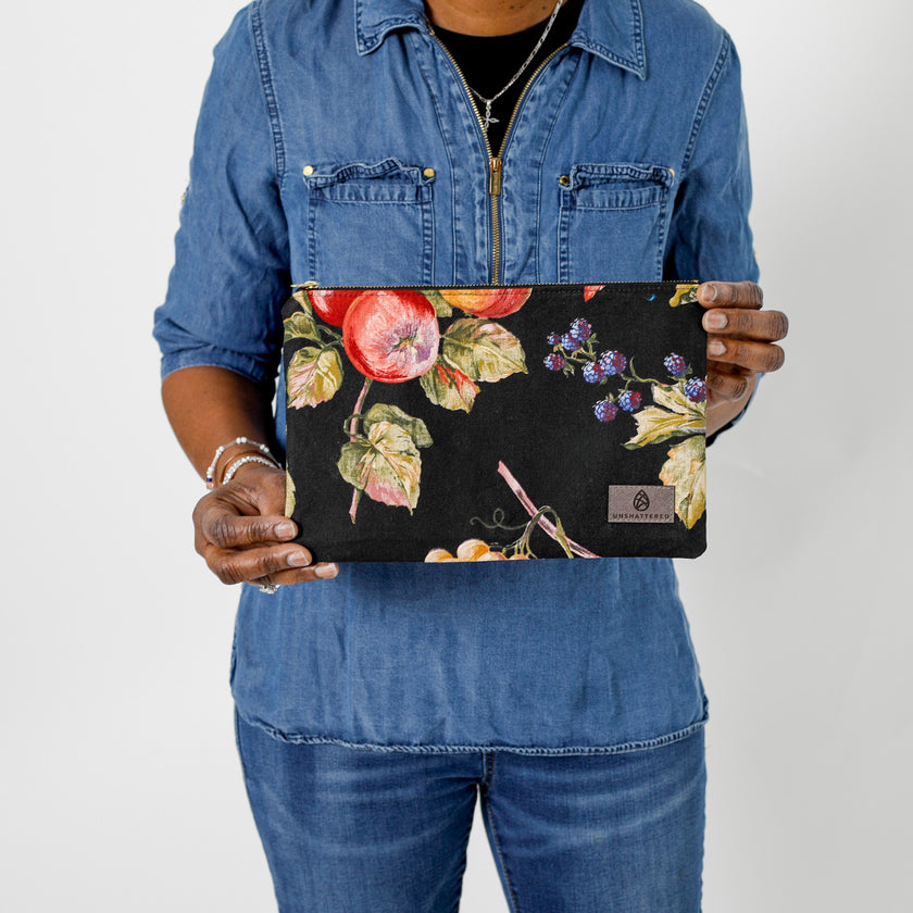 A woman holding a large black zip pouch with fruit and a gray label named after Diana