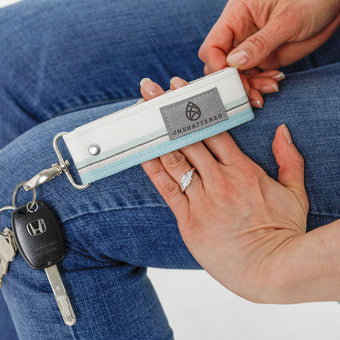 A hand holding white and blue striped key clip with keys named after Dymier 