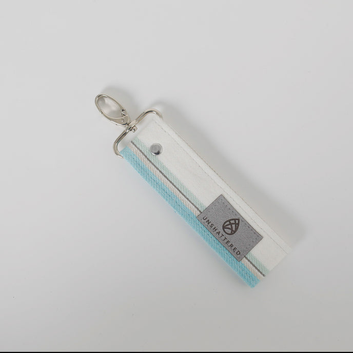 A white, gray, and blue striped key clip with a silver-push gate clip with gray Unshattered label named after Dymier