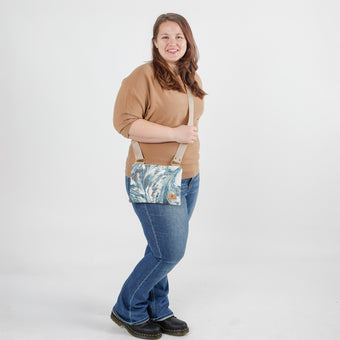 Woman holding a crossbody bag with a teal whisper microfiber pattern against a white background