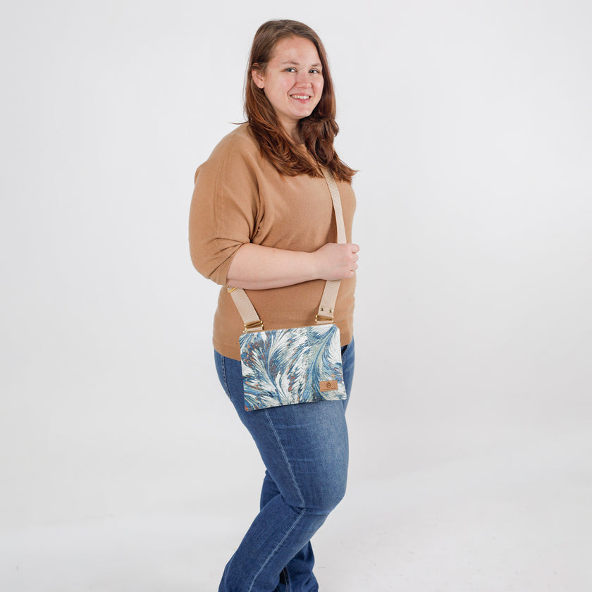 Woman wearing a crossbody bag with a teal whisper microfiber pattern on a white background
