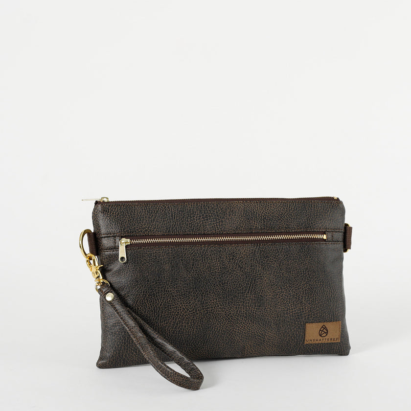 A brown 3-in-1 bag with a zipper closure, gold-tone hardware, and wristlet strap attached on a white background 