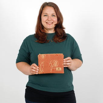 Person holding a small red/orange pouch with floral design against a white background named after Faith 
