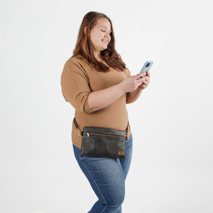 Woman wearing a brown waist bag and holding a phone on a white background