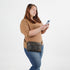 Woman wearing a brown waist bag and holding a phone on a white background