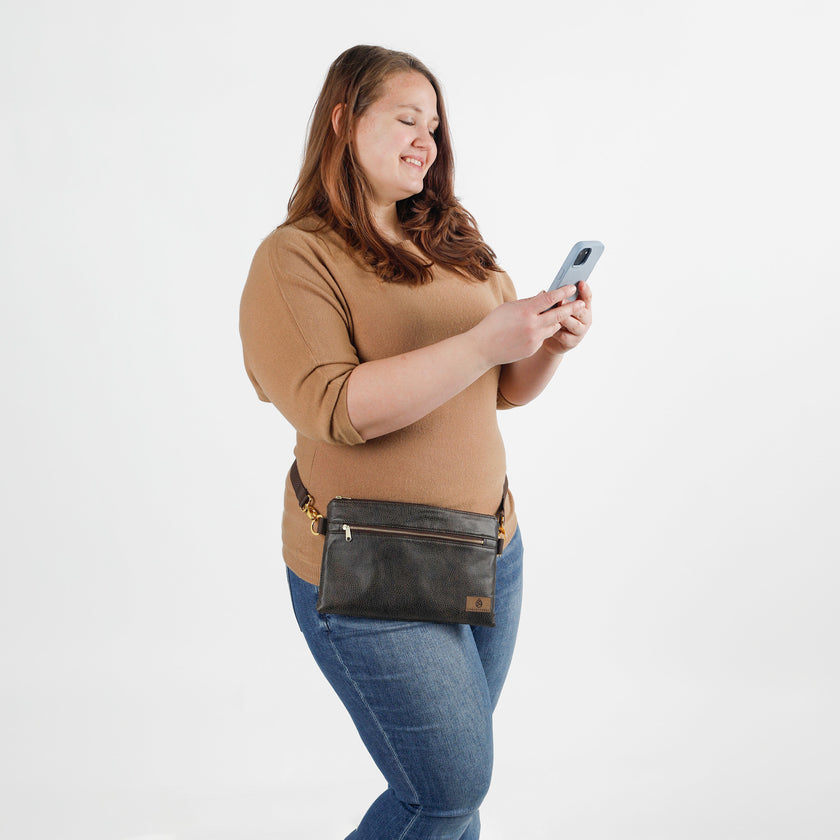 Woman wearing a brown waist bag and holding a phone on a white background