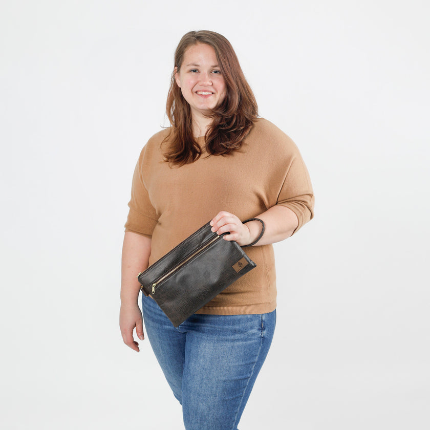 A woman holding a brown 3-in 1 wristlet bag against a white background