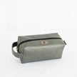 A gray toiletry kit with a zipper closure and a label displaying the brand name Unshattered named after Francine 