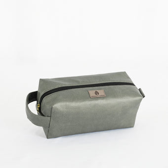 A gray toiletry kit with a zipper closure and a label displaying the brand name Unshattered named after Francine 