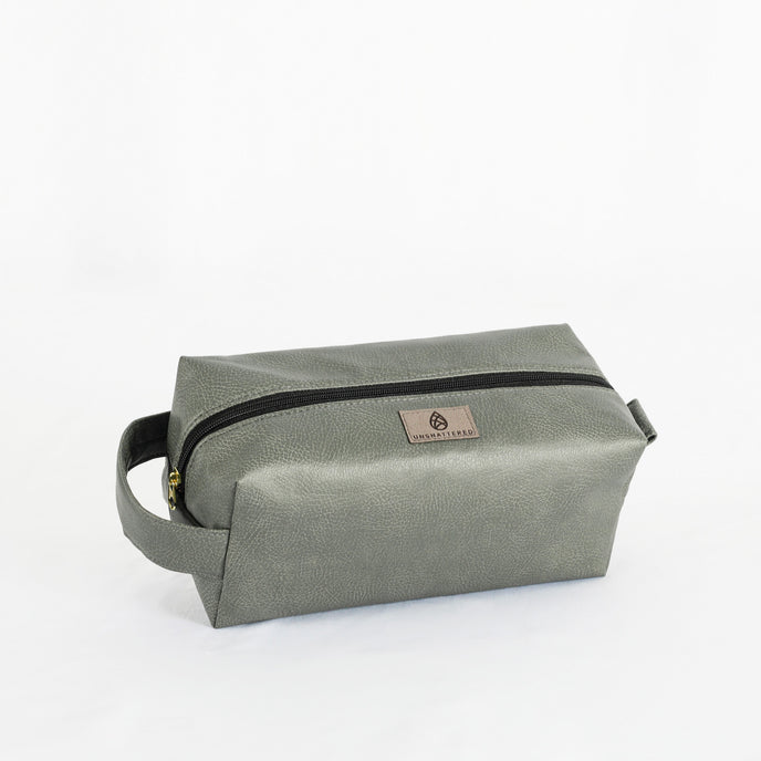 A gray toiletry kit with a zipper closure and a label displaying the brand name Unshattered named after Francine 