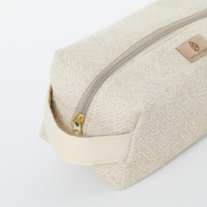 A gold tone zipper and cream luxury leather alternative handle on a beige toiletry kit 