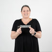 A woman smiling and holding this gray spotted key clip, featuring a subtle gray brand label and silver hardware.