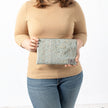 A woman holding a blue print design large zip pouch with a gray label and gold tone zipper
