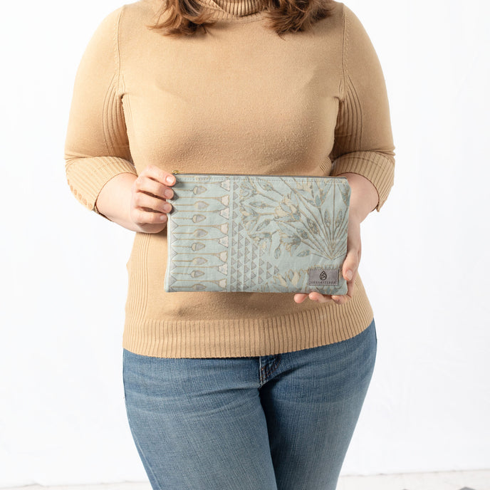 A woman holding a blue print design large zip pouch with a gray label and gold tone zipper